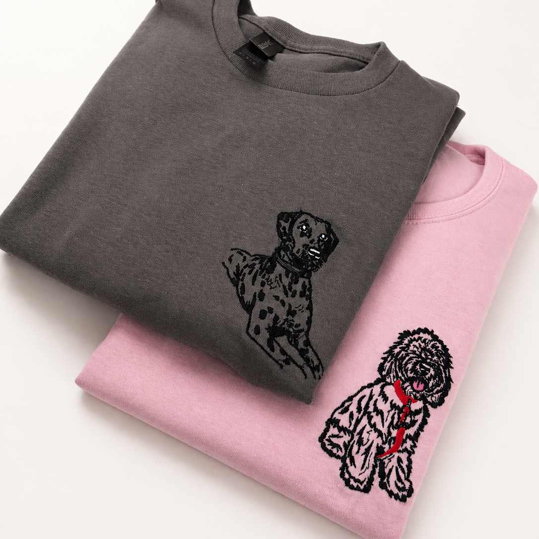 Two folded sweatshirts, one gray with a dog design and one pink with a different dog design, on a white background.
