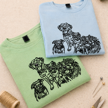Two folded sweatshirts, one green and one blue, with dog illustrations on a beige surface.