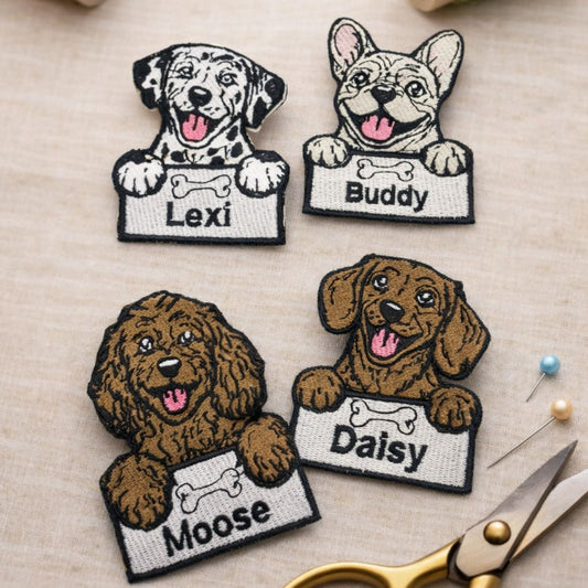 Four dog-themed patches with names on a crafting surface with scissors and thread.