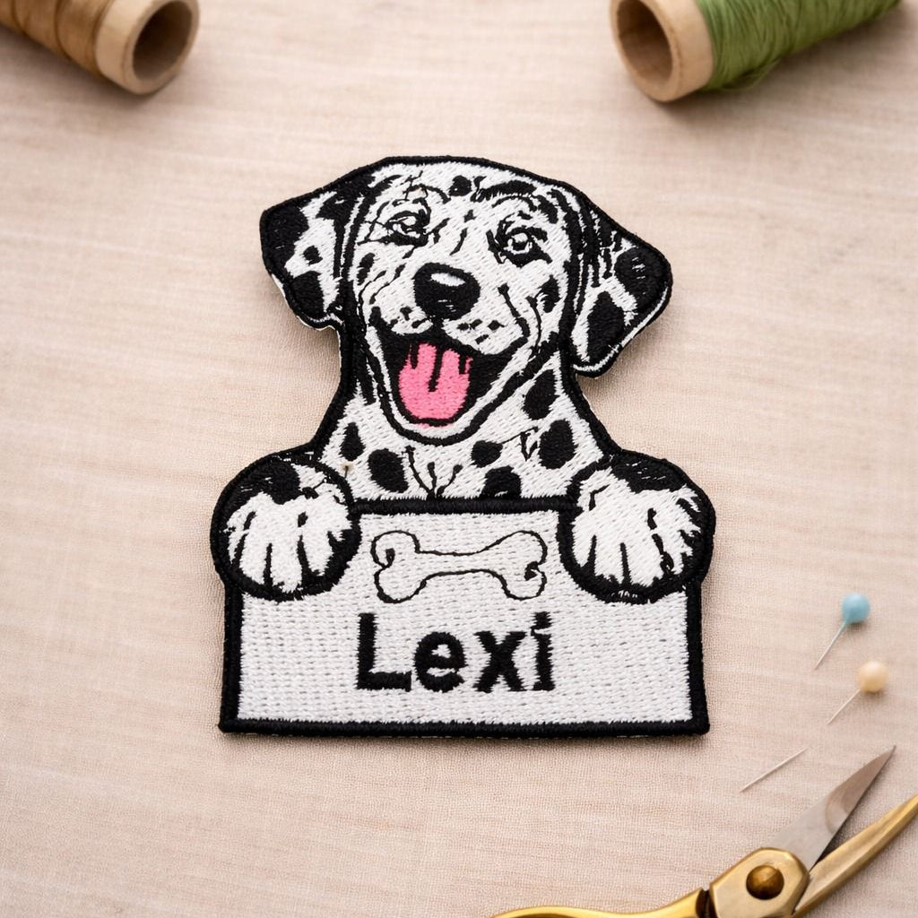 Embroidered patch of a dog holding a bone with 'Lexi' text, surrounded by sewing materials on a beige background.