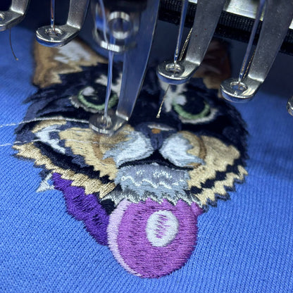 Cat on a blue background with embroidery needles working on the cat design 