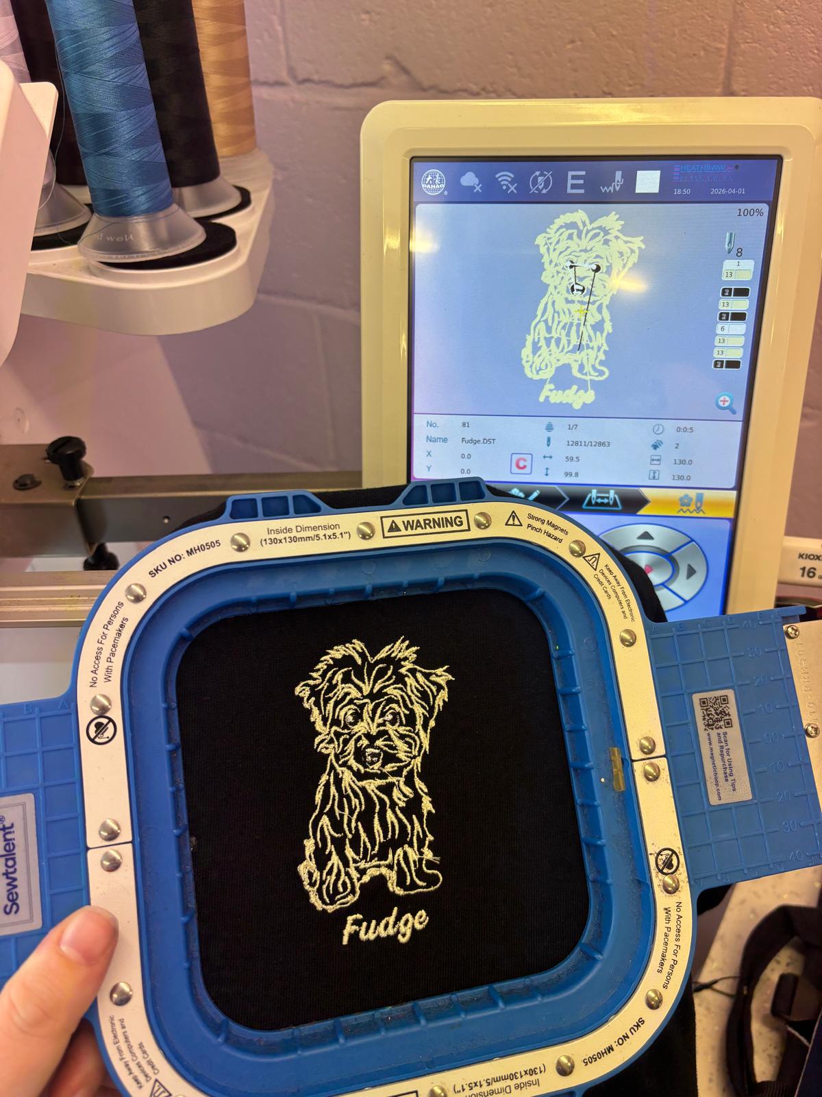 Embroidery machine with a digital display showing a design of a dog named 'Fudge'.