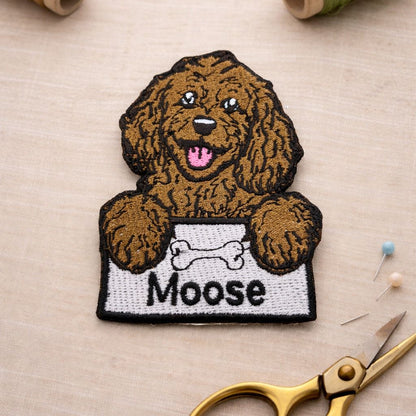 Embroidered patch of a dog named 'Moose' with sewing materials on a beige background