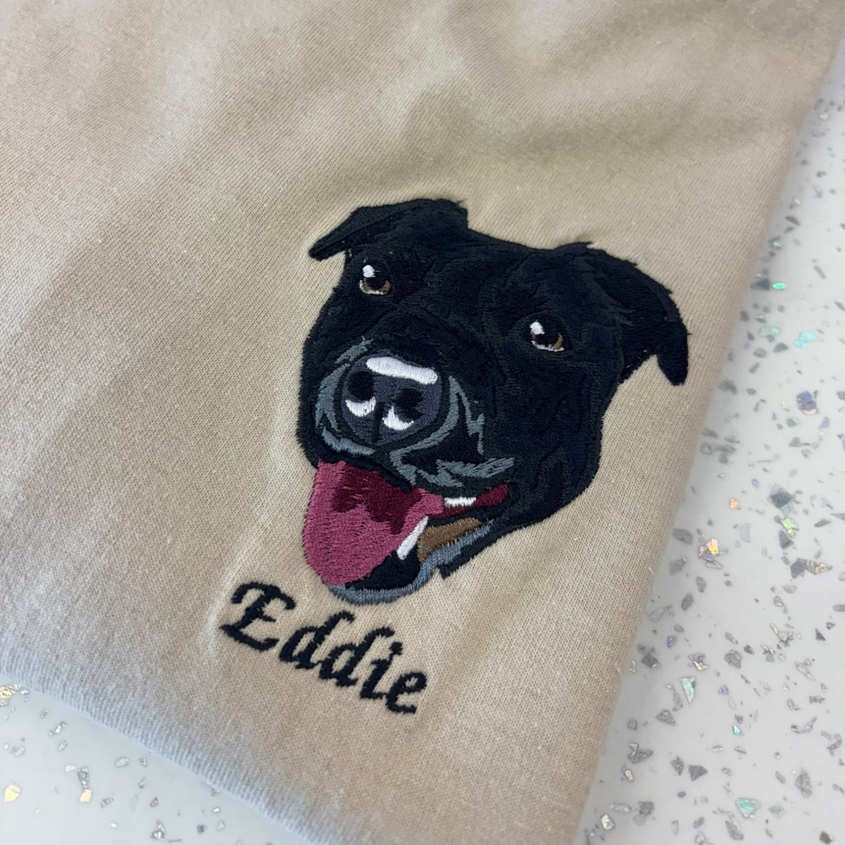 Beige sweatshirt with a black dog illustration and 'Eddie' text on a speckled surface
